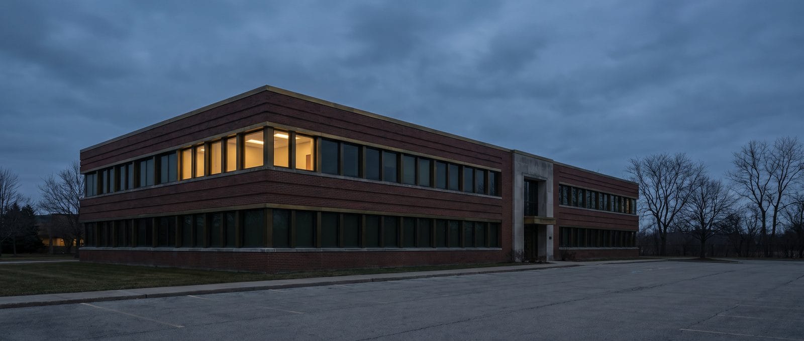 A low brick and glass office building at blue hour with light in the upper windows