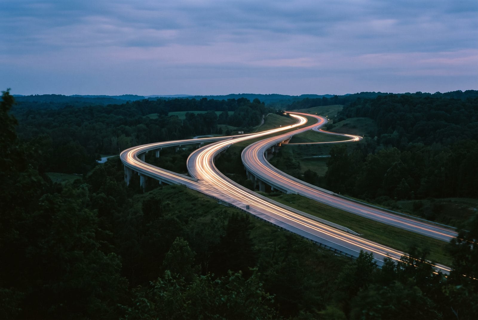 Two interstates merging seen from a ridge at dusk, drawn as ribbons of light