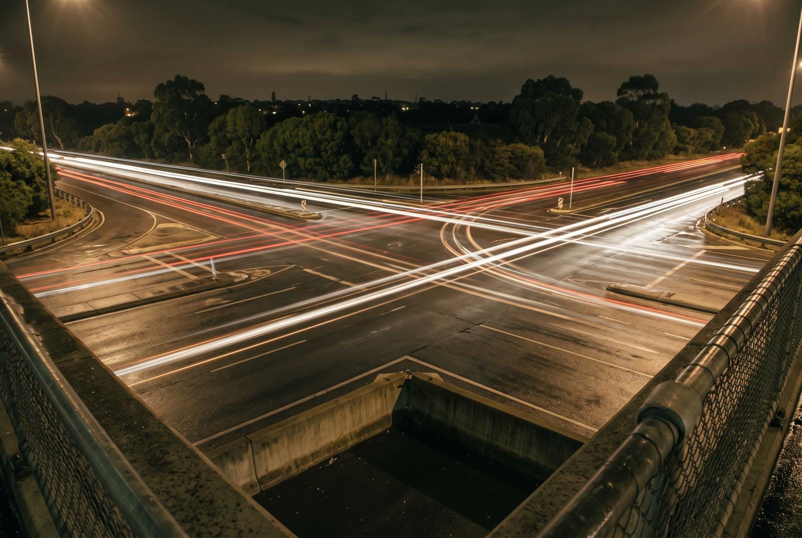 An intersection of two suburban roads from an overpass at night, light trails crossing