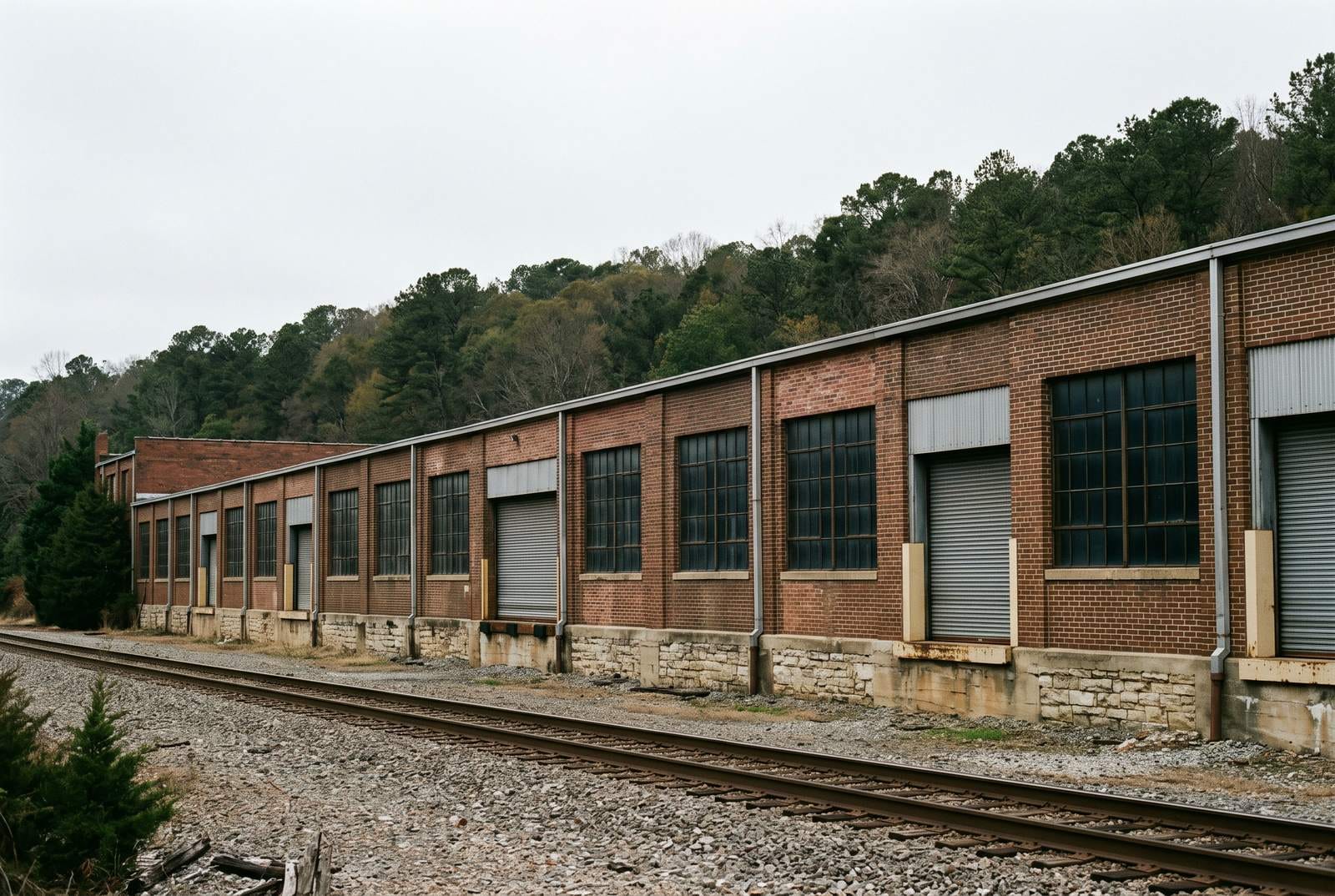 Low metal and brick warehousing beside a single railway track at first light