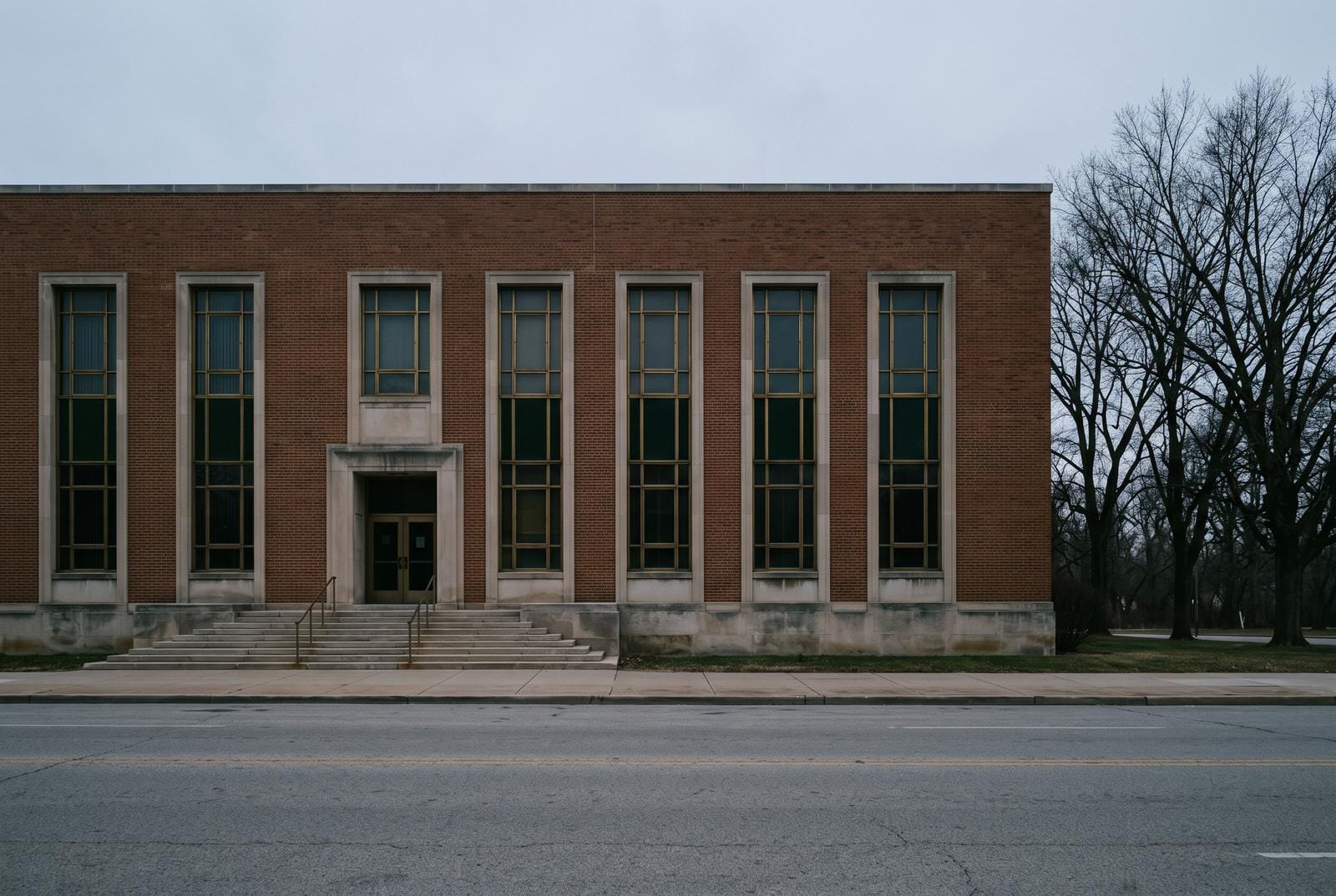 A plain limestone facade of nine tall windows seen from across an empty street